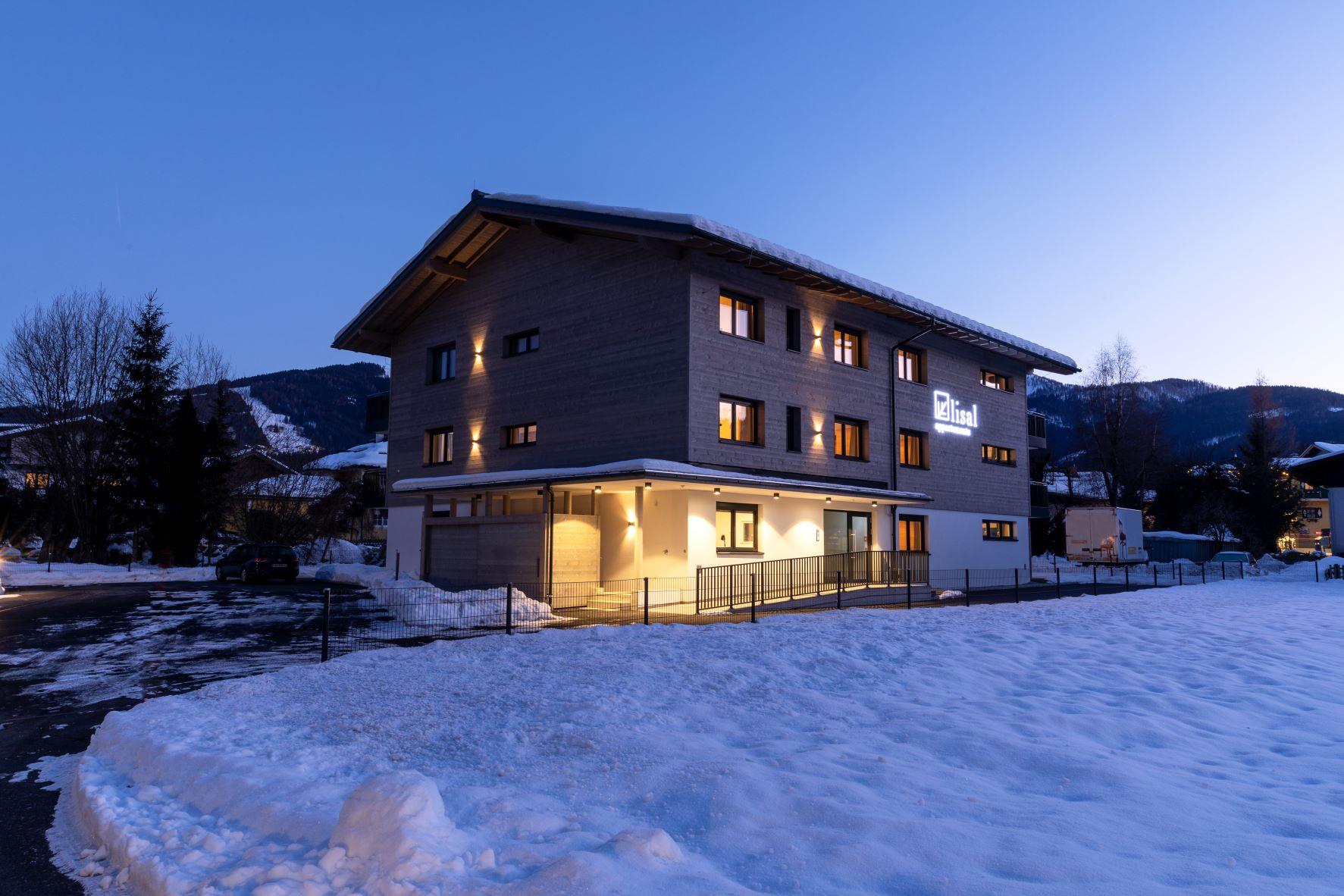 A modern building in the snow at dusk. The windows are brightly lit, giving the place a cozy atmosphere.