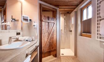 High-quality bathroom with a feel-good factor and daylight. This stylish bathroom combines alpine charm with modern comfort. The walk-in shower with glass partition, warm natural stone tiles, and elegant wood details create a cozy atmosphere. A spacious washbasin with illuminated cosmetic mirror and hairdryer ensures comfort in everyday life – perfect for relaxed moments after an active day in the mountains.
