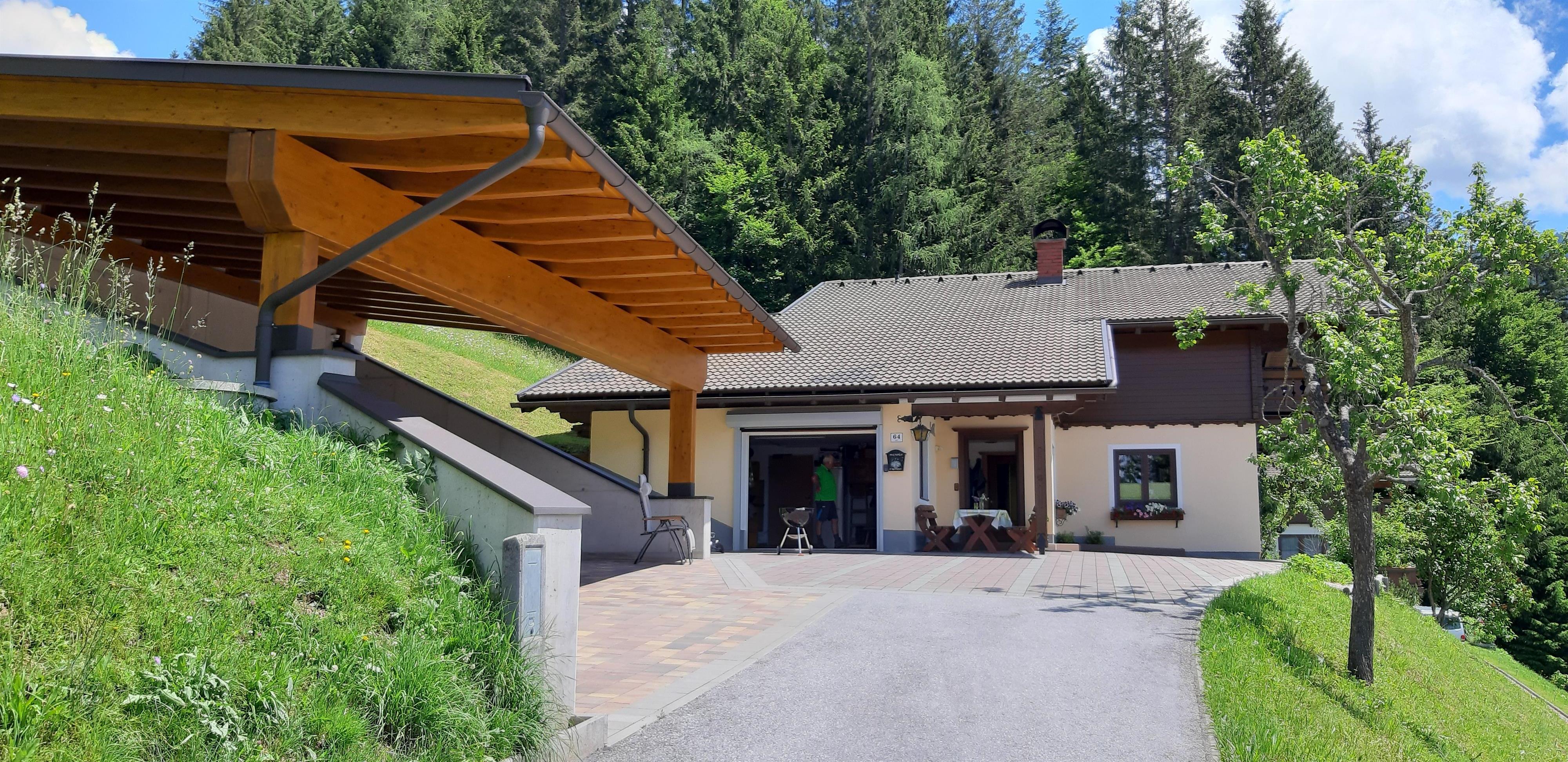 A beautiful house surrounded by trees and a green meadow. The entrance is protected by a covered area.