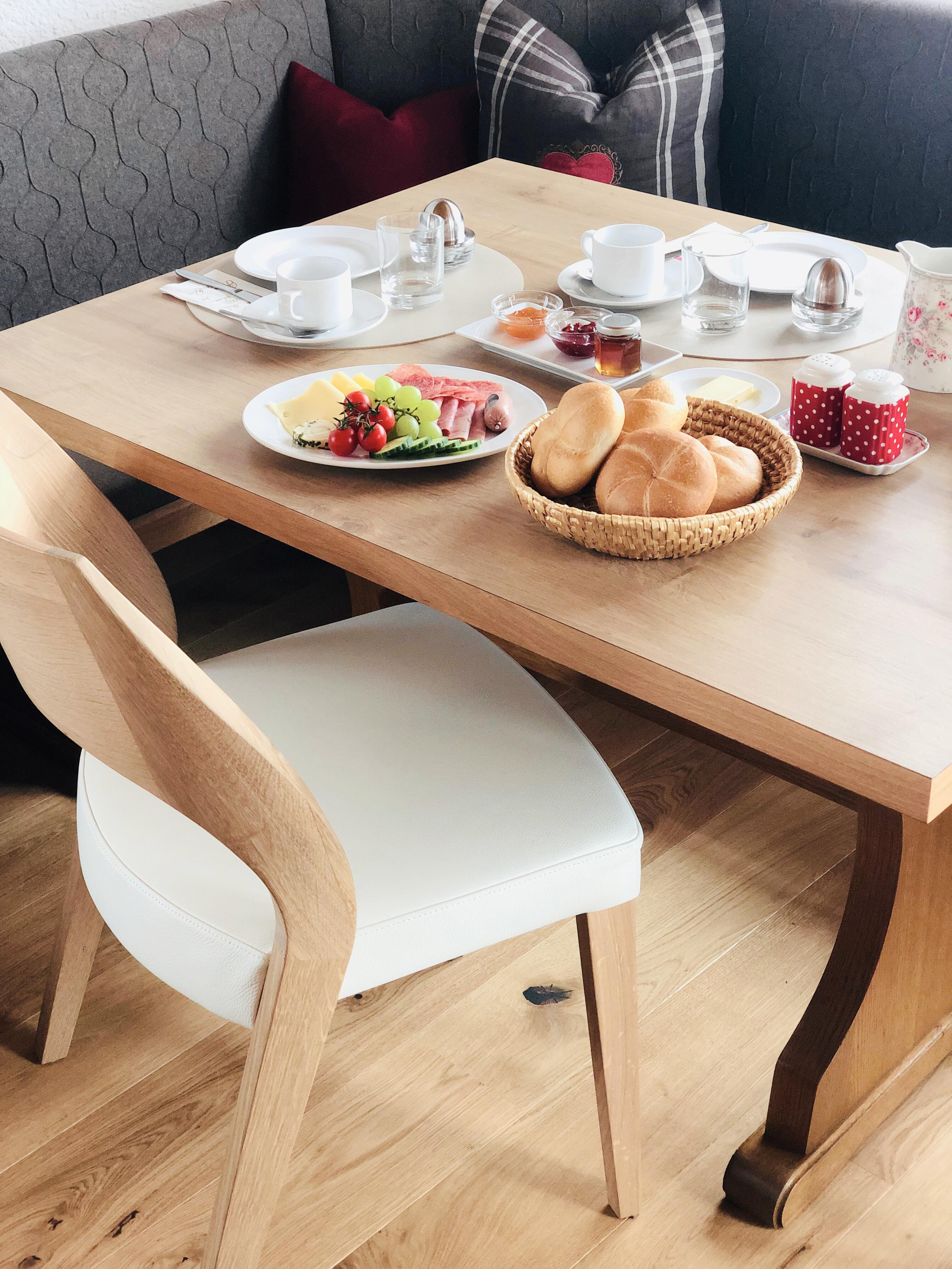 A beautiful table set with breakfast. There are fresh rolls, cold cuts, fruit, and drinks.