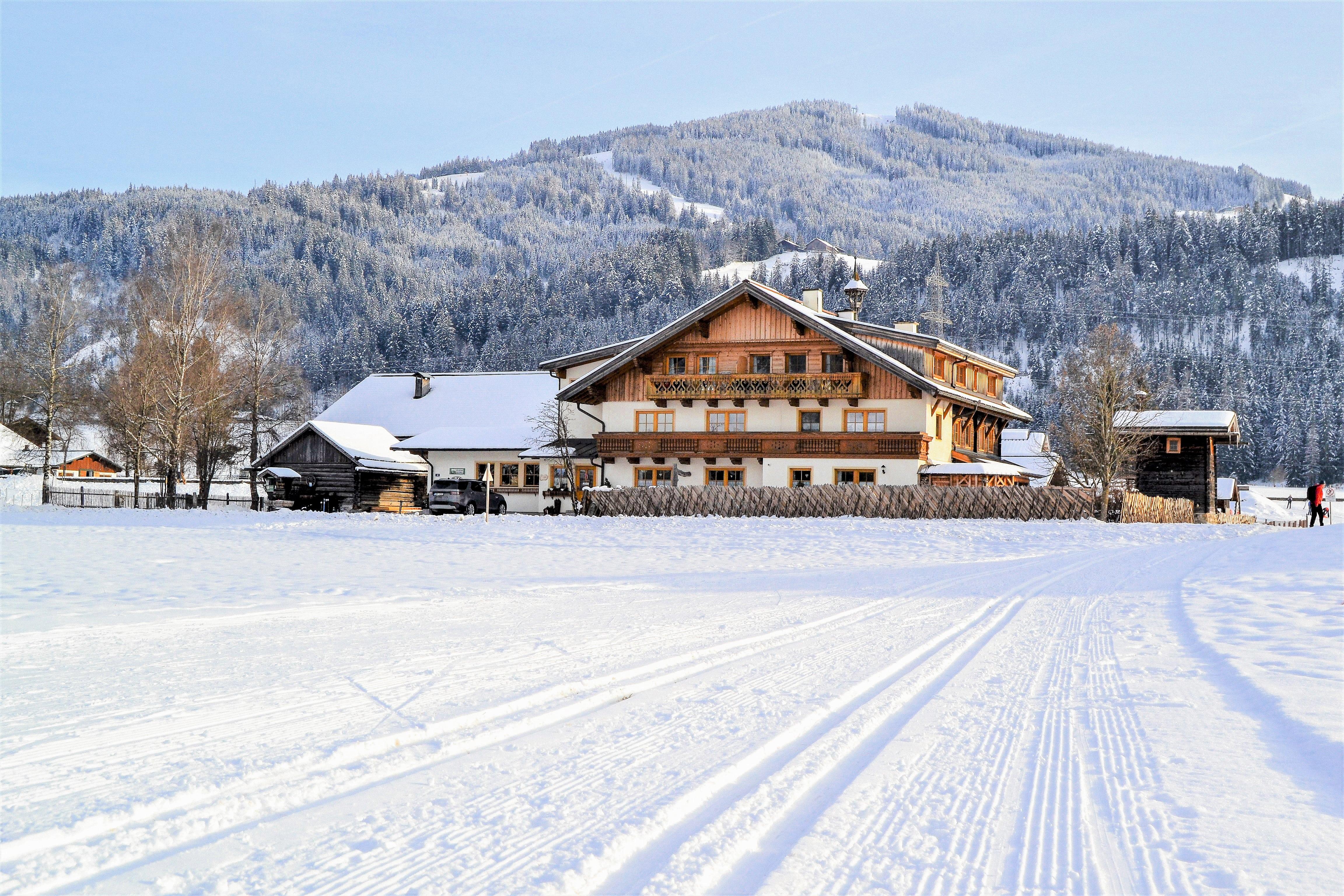 A beautiful, snow-covered house in a wintry landscape. The surrounding mountains are covered in snow and the sky is clear.