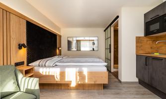 A modern room with a comfortable bed and a kitchenette. The bright colors and wood design create an inviting atmosphere.