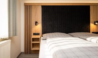 A modern bedroom with a double bed and stylish wooden paneling. The soft lighting creates a cozy atmosphere.