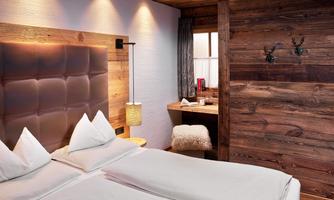 Stylish bedroom with chalet flair. This cozy bedroom combines elegant design with alpine charm. Warm rustic wood paneling, a padded leather headboard, and soft lighting create a comfortable atmosphere. The high-quality craftsmanship and natural materials create a place of tranquility and relaxation – ideal for restful nights amidst the mountains.