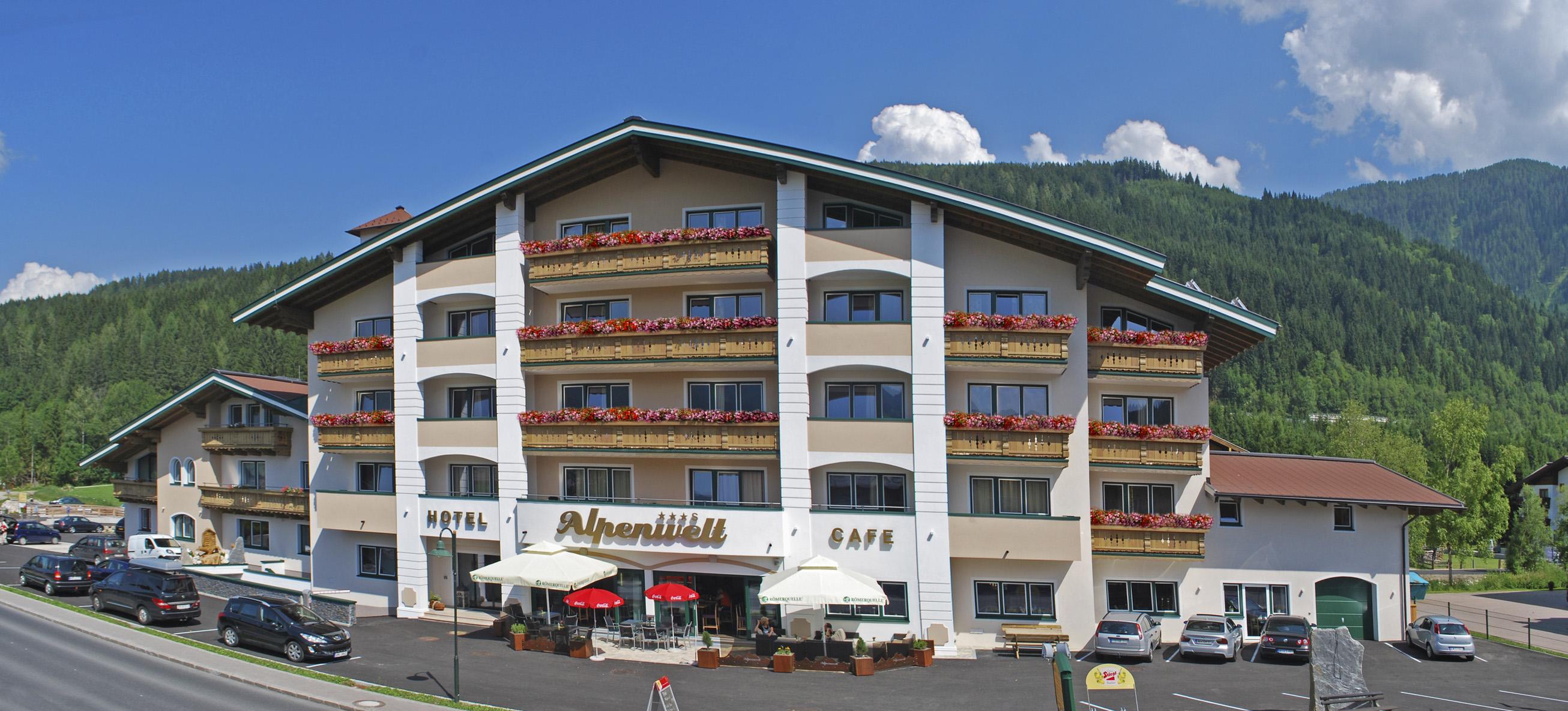 A modern hotel building with several floors and beautiful balconies. Surrounded by green hills and a clear blue sky.