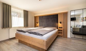 A modern bedroom with a wooden bed and cozy furnishings. Large windows provide plenty of daylight and a pleasant atmosphere.