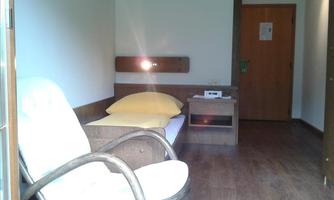 A simple room with a comfortable armchair and a bed. The walls are light and the floor has a wood look.