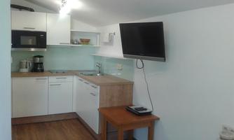 A modern kitchen with white furniture and wooden countertops. There is a television, a kettle, and a coffee maker.