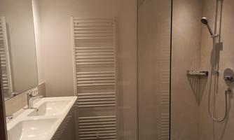 A modern bathroom with a large shower and a sink. The walls are light, and there is a towel radiator.