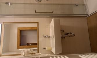 A modern bathroom with a sink, a large mirror, and a shower. The walls are brightly tiled and the floor has a wood look.