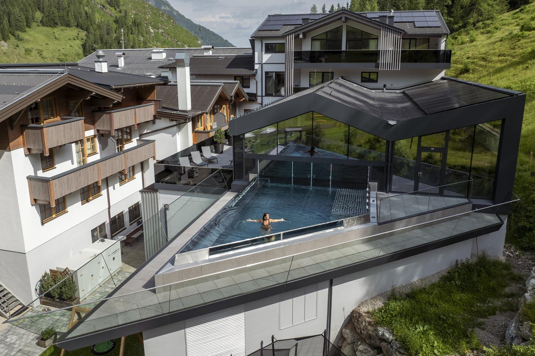 A modern building with a covered pool area. In the background, green mountains and additional luxurious accommodations can be seen.