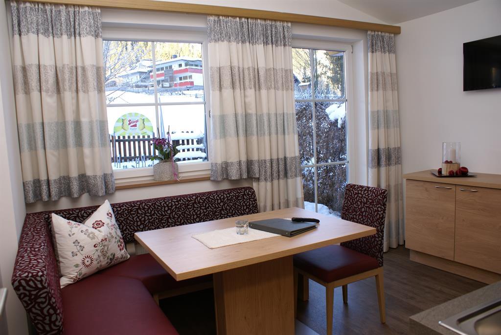 A cozy dining area with a wooden bench and a table. Large windows let in plenty of daylight and offer a view of the snowy landscape.