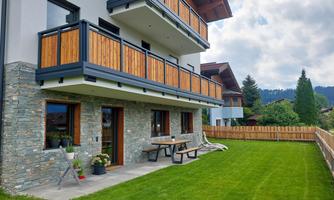 A modern house with a wooden balcony and a well-maintained garden. The surroundings are green and offer plenty of space to relax.