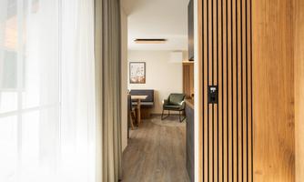 A modern interior with wooden paneling and a view of the cozy dining area. Light streams through the windows, creating an inviting atmosphere.