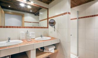 Bright bathroom with double sink<br/>The welcomingly designed bathroom offers ample space for relaxed morning routines with a generous double sink. Bright tiles combined with warm natural tones and rustic wood elements create a pleasant atmosphere. Equipped with a cosmetic mirror, hairdryer, fresh towels, and stylish lighting, this bathroom leaves nothing to be desired. The adjoining shower with a glass door perfectly complements the modern comfort in a traditional setting.