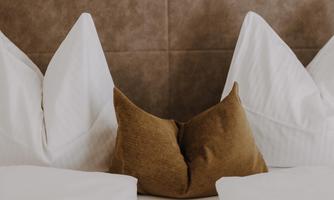 A cosy bed with white pillows and a brown decorative pillow.