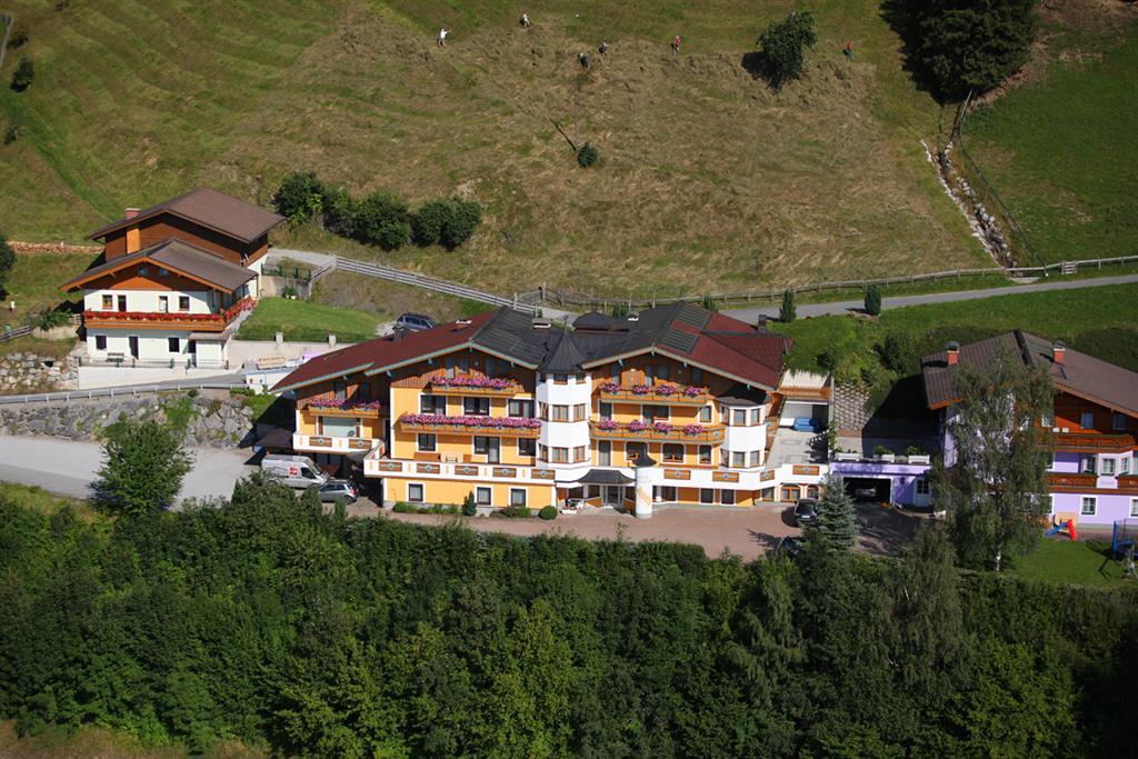 A picturesque view of a hotel amidst green hills. The buildings are rustic in design and surrounded by trees.