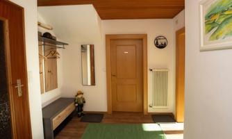 A friendly hallway with a wooden panel, a coat rack, and a mirror. On the right is a heater and a painted picture on the wall.