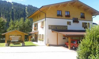 A charming alpine building with rooms and vacation apartments. The surroundings are green and surrounded by mountains.
