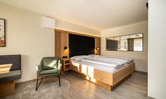 A modern bedroom with a double bed and a cozy seating area. There is a large mirror and bright wood that makes the space feel inviting.