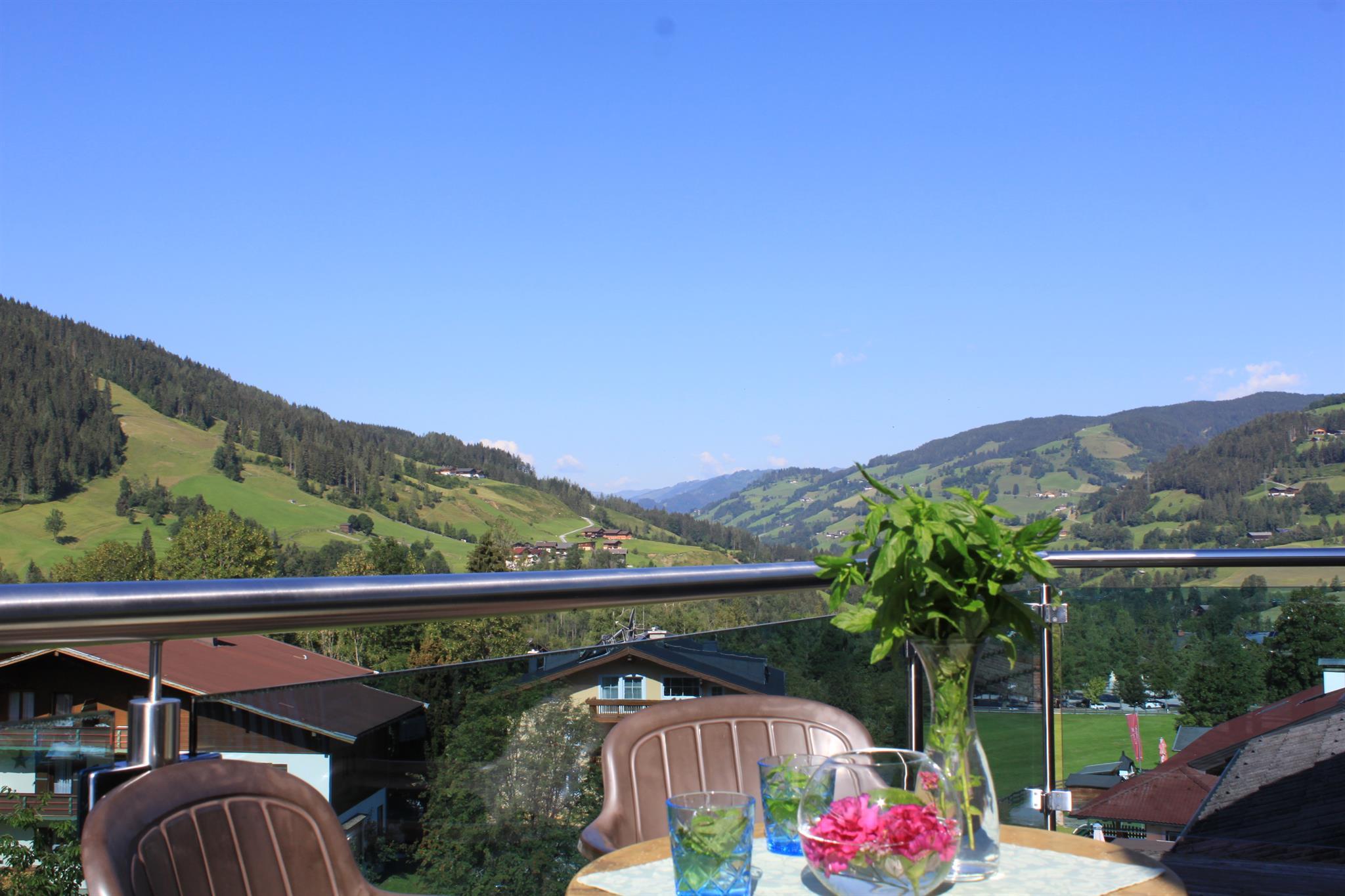 A beautiful view from a balcony of green hills and mountains. There are flowers and drinks on the table.