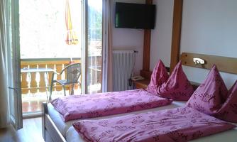 A cozy room with a double bed and pink pillows. The balcony offers a view of the outdoors.