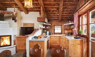 Alpine charm meets coziness – Your dream kitchen with a fireplace. Immerse yourself in the warm ambiance of this cozy country-style kitchen in alpine design. The centerpiece of the room is the open fireplace, which not only provides comforting warmth but is also a real highlight for cozy evenings. Rustic wooden beams on the ceiling, natural materials, and lovingly crafted details create a snug atmosphere that invites you to linger. The fully equipped kitchen offers modern comfort with traditional elements. A television allows for relaxed cooking with entertainment. Large windows provide a magnificent view of the surrounding mountain landscape. Whether cooking, dining, or simply enjoying the fire – this kitchen combines tradition with functionality and offers an authentic Alpine living experience.