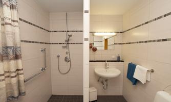A modern bathroom with a shower on the left side and a sink on the right side. The walls are tiled in light colors and equipped with a towel holder.