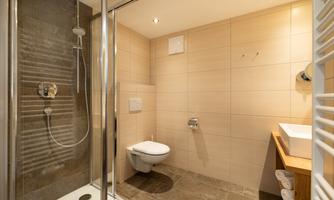 A modern bathroom with a shower and a toilet. The walls are painted in neutral colors and there is a vanity and towel warmer. The towels are provided for the holiday.