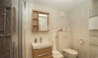 A modern bathroom with a shower and a stylish sink. The walls are light and minimally designed.