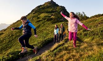 A group of children is happily hiking up a hill. The sun is rising and illuminating the landscape.