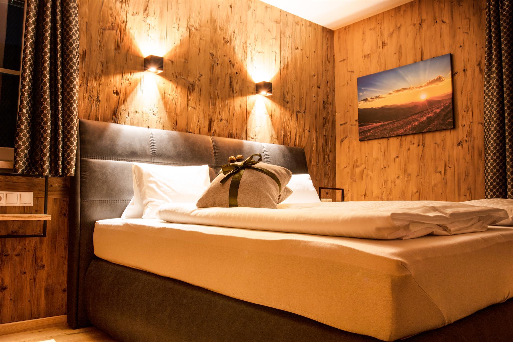 A cozy bedroom with warm wooden paneling and soft lighting. The bed is inviting and adorned with decorative pillows.
