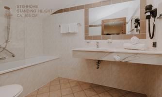 A modern bathroom with a bathtub and a sink made of marble. Please note that in the bathtub with hand shower there is only a standing height of approx. 165 cm.