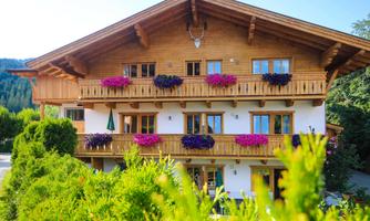 A pretty wooden house with balconies and gardens.  
Surrounded by green grass and trees in a picturesque landscape.