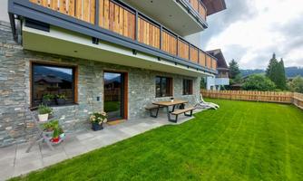 A modern terrace with a well-maintained garden and a view of the mountains. There is a table and chairs, perfect for relaxing hours outdoors.