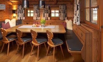 Quaint and cozy room with a large dining table. In this traditional room, with great attention to detail, alpine charm meets homely coziness. The large wooden table with handmade chairs and surrounding corner bench provides space for sociable hours with family and friends. Warm wood tones, atmospheric lighting, and loving accents such as pillows, curtains in deer design, and natural materials make this space the heart of the chalet – perfect for shared meals and cozy evenings.