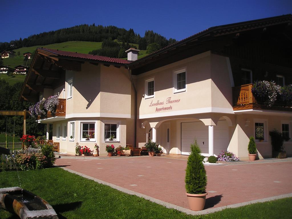 A charming country house with blooming flowers and a well-maintained garden. In the background, green hills can be seen.