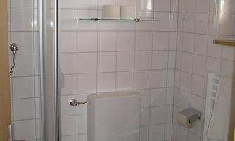 A small bathroom with a shower and toilet. The walls are tiled with white tiles.