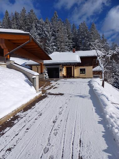 A snow-covered house in the mountains. The path is marked with footprints in the snow, and in the background, there are snow-covered trees.