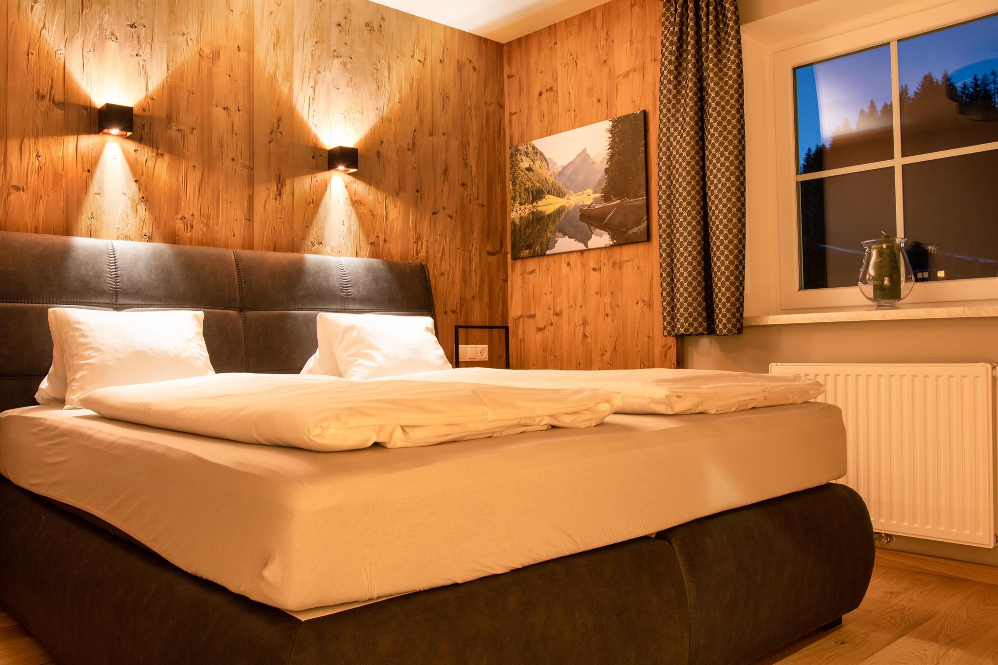 A cozy bedroom with a large bed and wooden walls. Soft lighting creates a relaxed atmosphere.