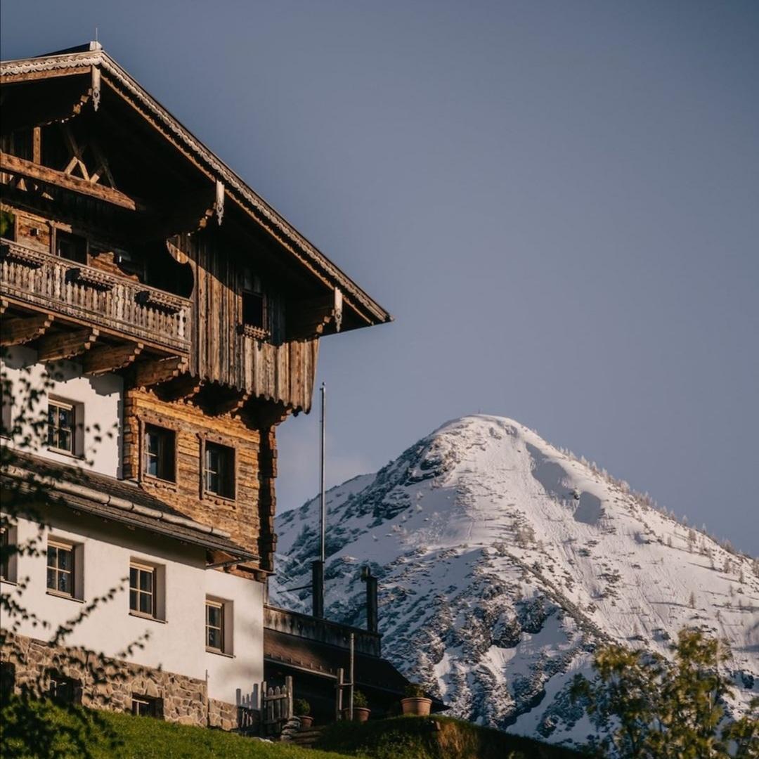 A traditionally designed mountain architecture with great attention to detail, featuring old wood cladding in the foreground. In the background, a snow-covered peak rises.