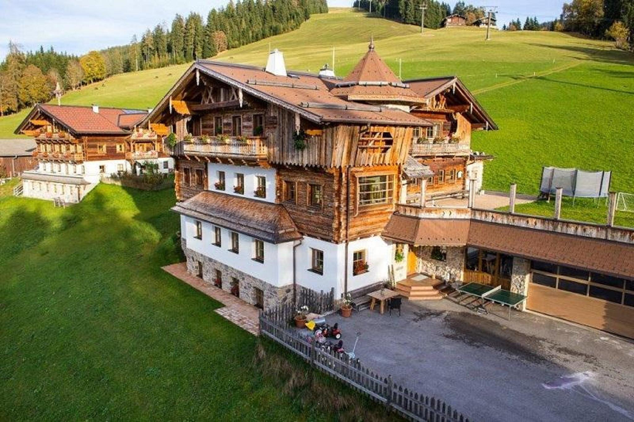A house designed with great attention to detail, clad in old wood, set in an idyllic green landscape. In the background, gentle hills and forests can be seen. Holiday apartments in the mountains. Get away from everyday life, take a deep breath, and immerse yourself in the pure experience of nature. While staying in the mountains.