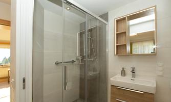 A modern bathroom with a glass shower enclosure and wooden shelves. The sink has an elegant faucet and a large mirror.