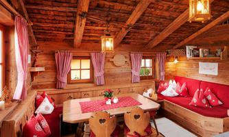 Alpine charm with heart – coziness to arrive and feel at home. Step into our lovingly furnished cabin and feel immediately: Here is a temporary home. In our rustic parlor with traditional wooden furniture, red heart decor, and warm light, you will experience true alpine coziness. Whether at breakfast at the large wooden table, reading on the cozy corner sofa, or playing with the family – this space invites you to linger. Red cushions, traditional checkered curtains, and handcrafted details create a comfortable atmosphere that can only be found in a real alpine hut. A place to unwind, enjoy, and be together – exactly what a true cabin vacation is all about.
