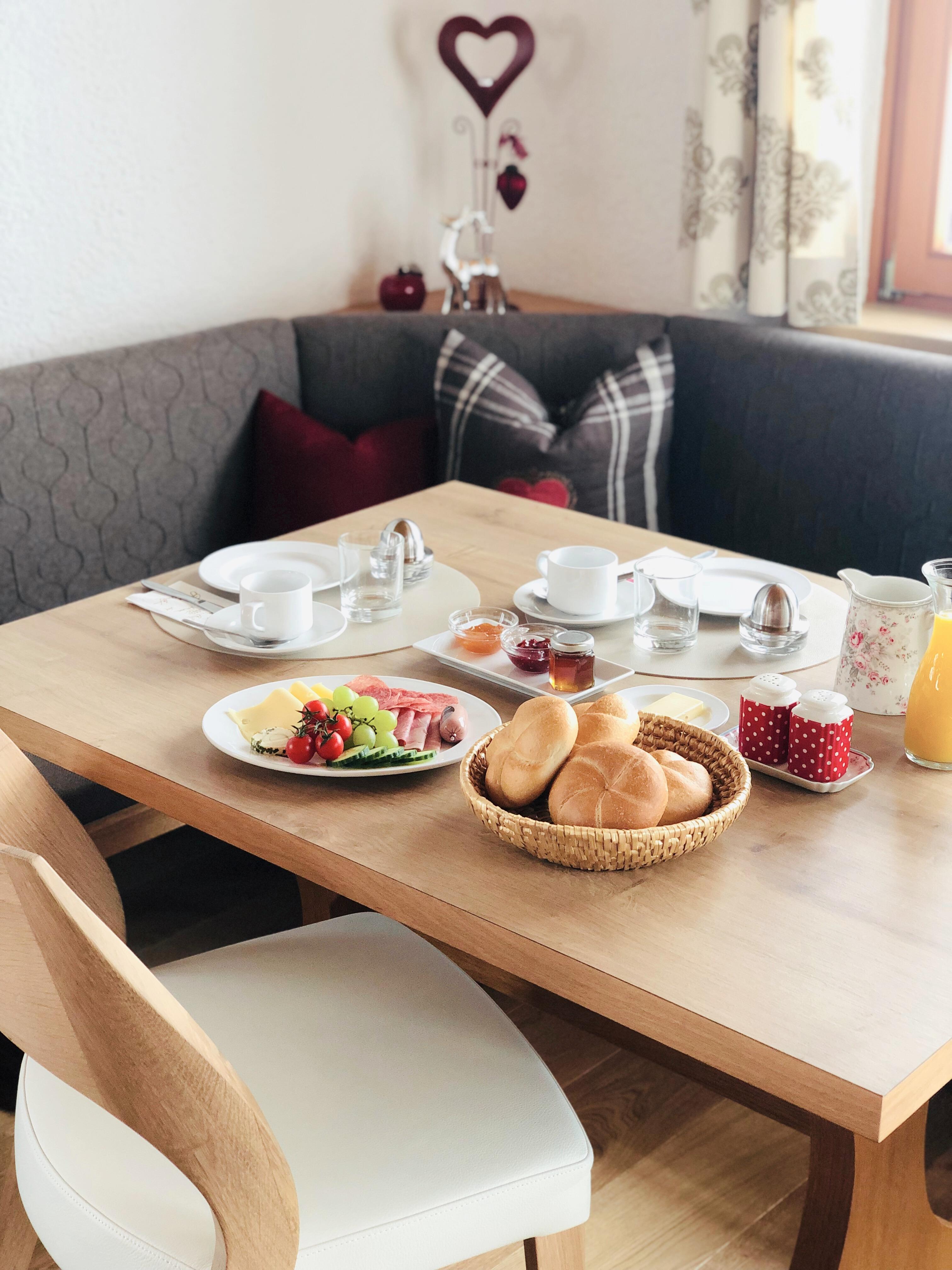 A cozy table with a delicious breakfast. There are fresh rolls, fruit, and drinks in an inviting setting.