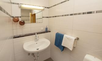 A modern bathroom with a sink and a large mirror. It features bright tiles and fresh towels.