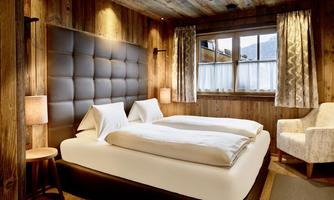 High-quality bedroom with cozy chalet flair. This stylishly furnished bedroom combines natural materials with modern comfort. The large double bed ensures restful nights, while warm wooden walls, subtle lighting, and elegant curtains create a cozy atmosphere. A comfortable armchair by the window invites reading or resting – ideal for relaxed hours after an active day in the mountains.
