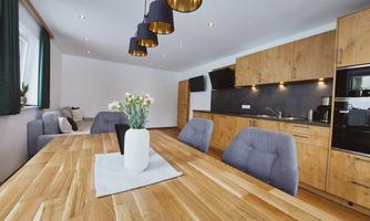 A bright dining area with a large wooden table and elegant chairs. The modern kitchen in the background is well-equipped and feels inviting.