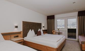 A modern hotel room with a double bed, a single bed, a sofa bed, and cosy wooden decorative elements.