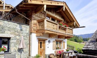 Chalet with alpine charm and a view of greenery! This stylish front view of our chalet shows the perfect combination of natural stone, reclaimed wood, and loving details. The carved wooden balconies, traditional shutters, and colorful flower boxes give the house its distinctive character. On the spacious sun terrace with a bench, wooden table, and barbecue facilities, the mountain world can be enjoyed to the fullest. A place to arrive and feel comfortable – right in the middle of nature.